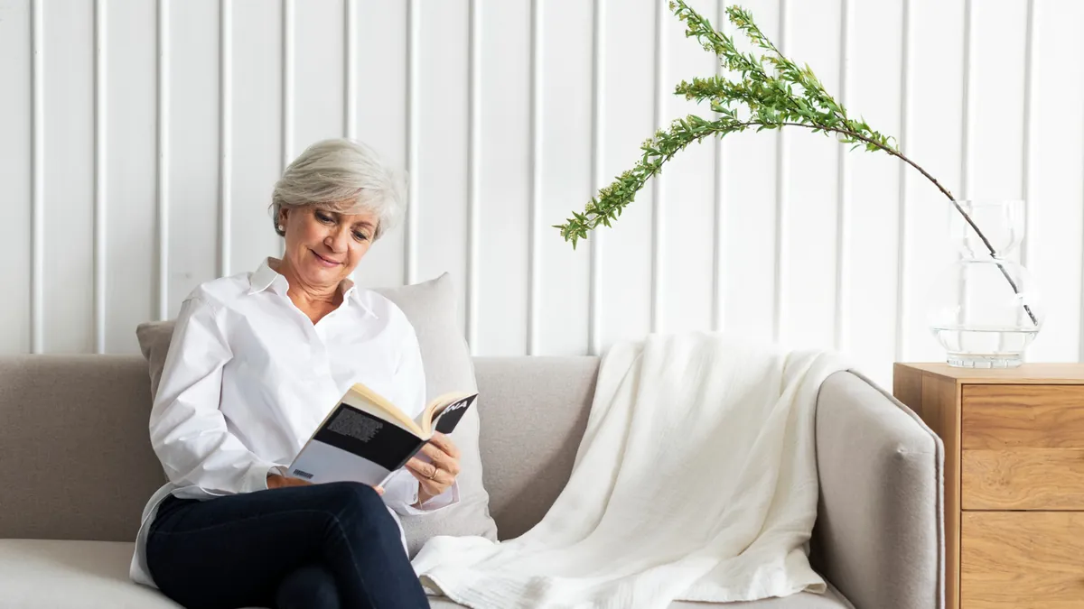 Older woman reading a book while relaxing on a sofa in a bright living room
