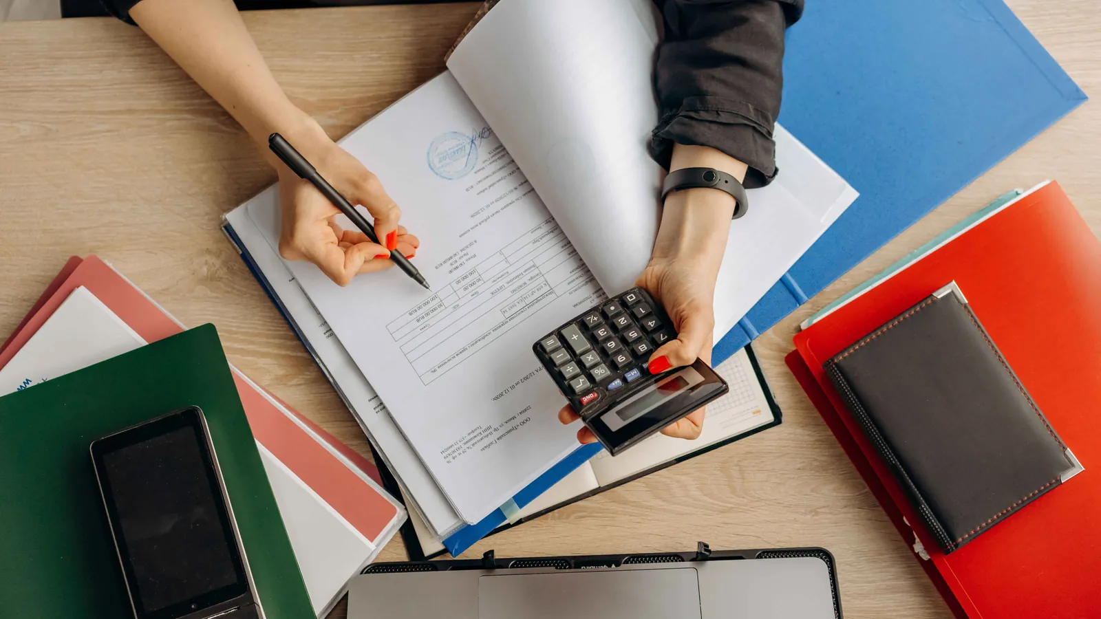 Personne examinant des documents avec un stylo et une calculatrice à son bureau