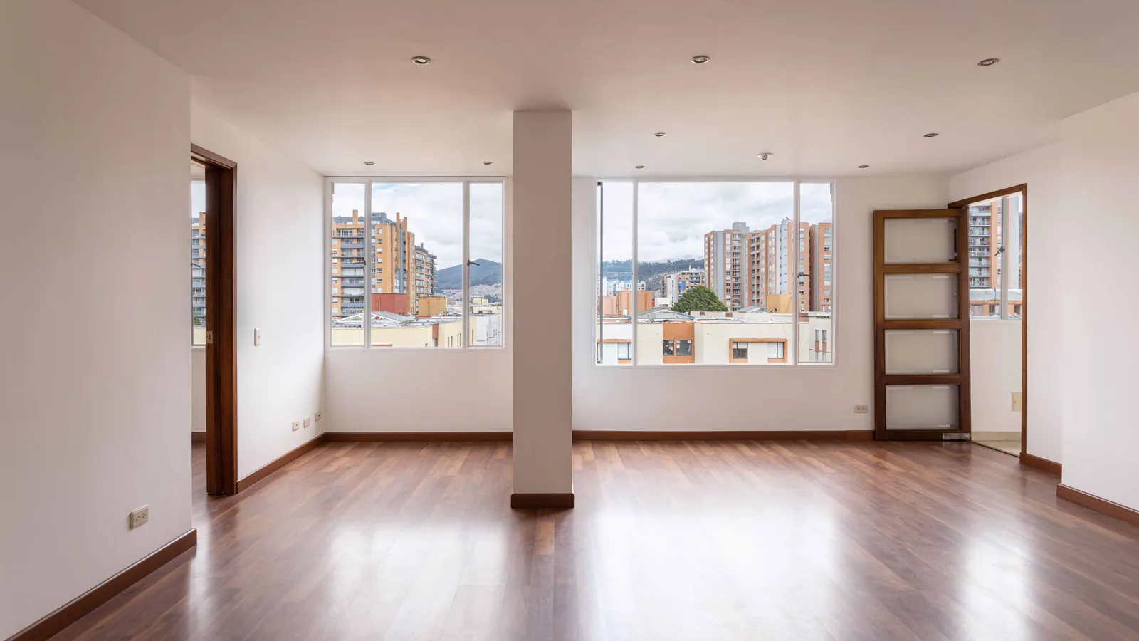 Appartement vide avec un plancher de bois, des murs blancs et de grandes fenêtres avant l’emménagement