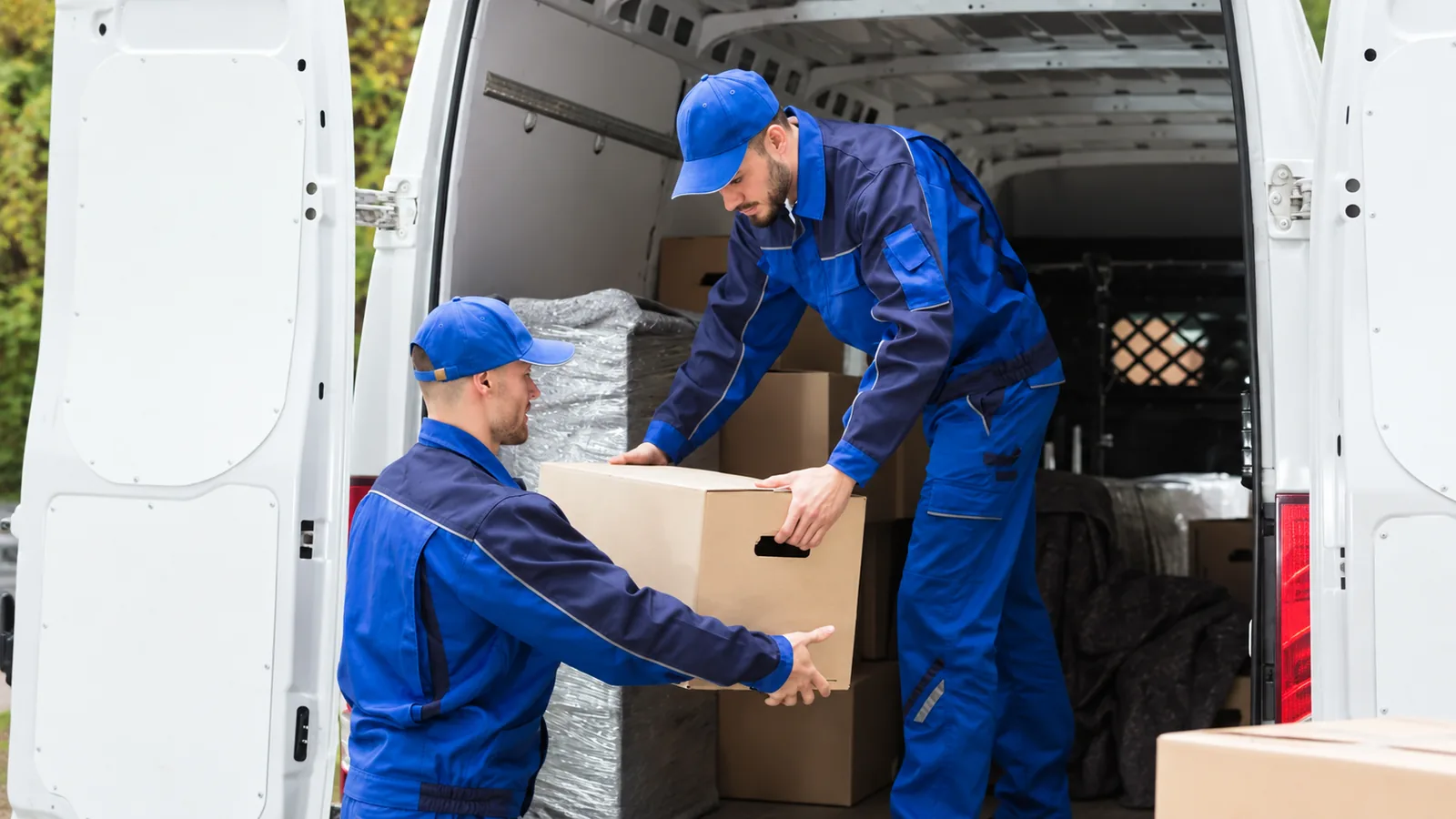 Deux déménageurs en uniforme bleu chargent une boîte dans un camion
